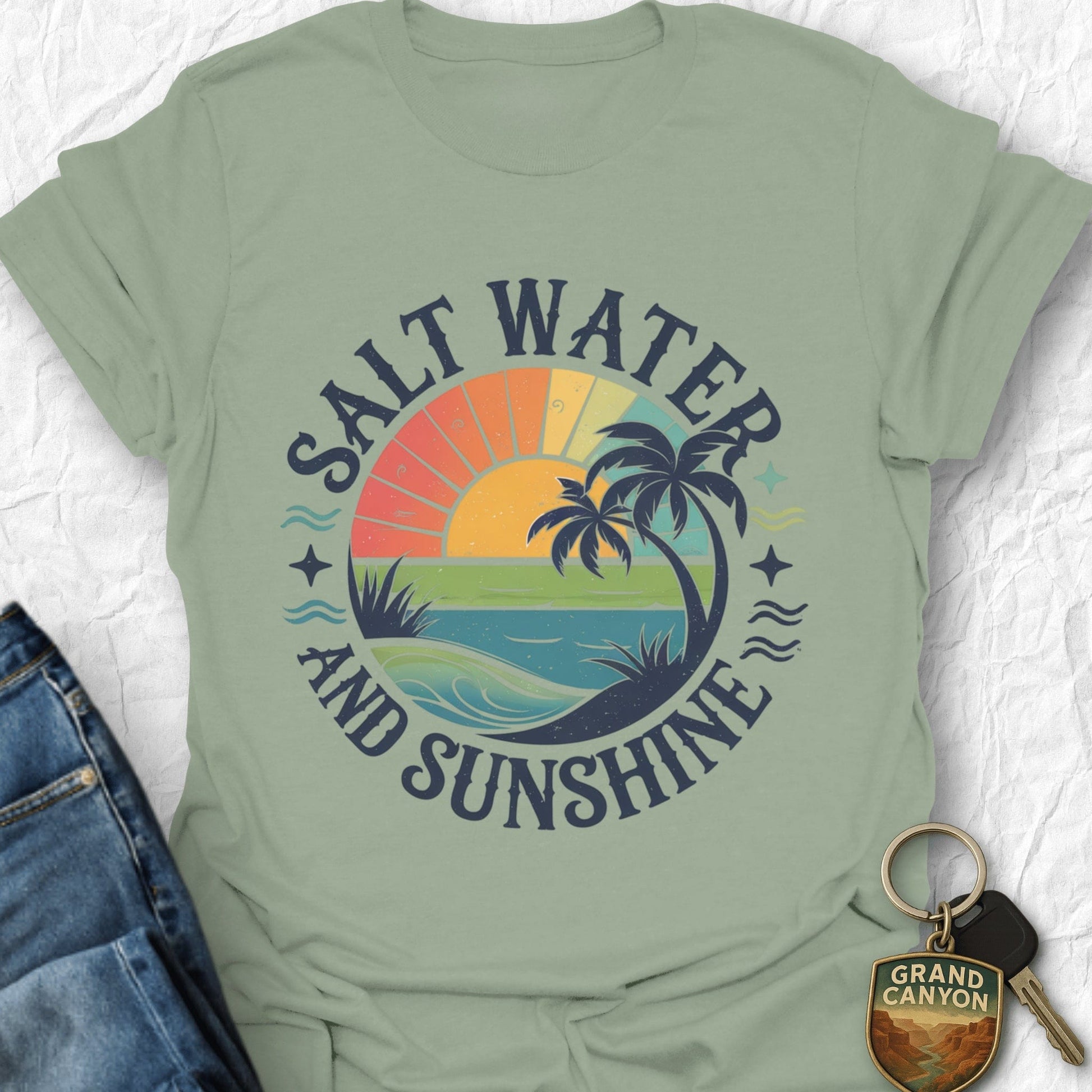 Sage green t-shirt with 'Salt Water and Sunshine' graphic design on a textured white background.