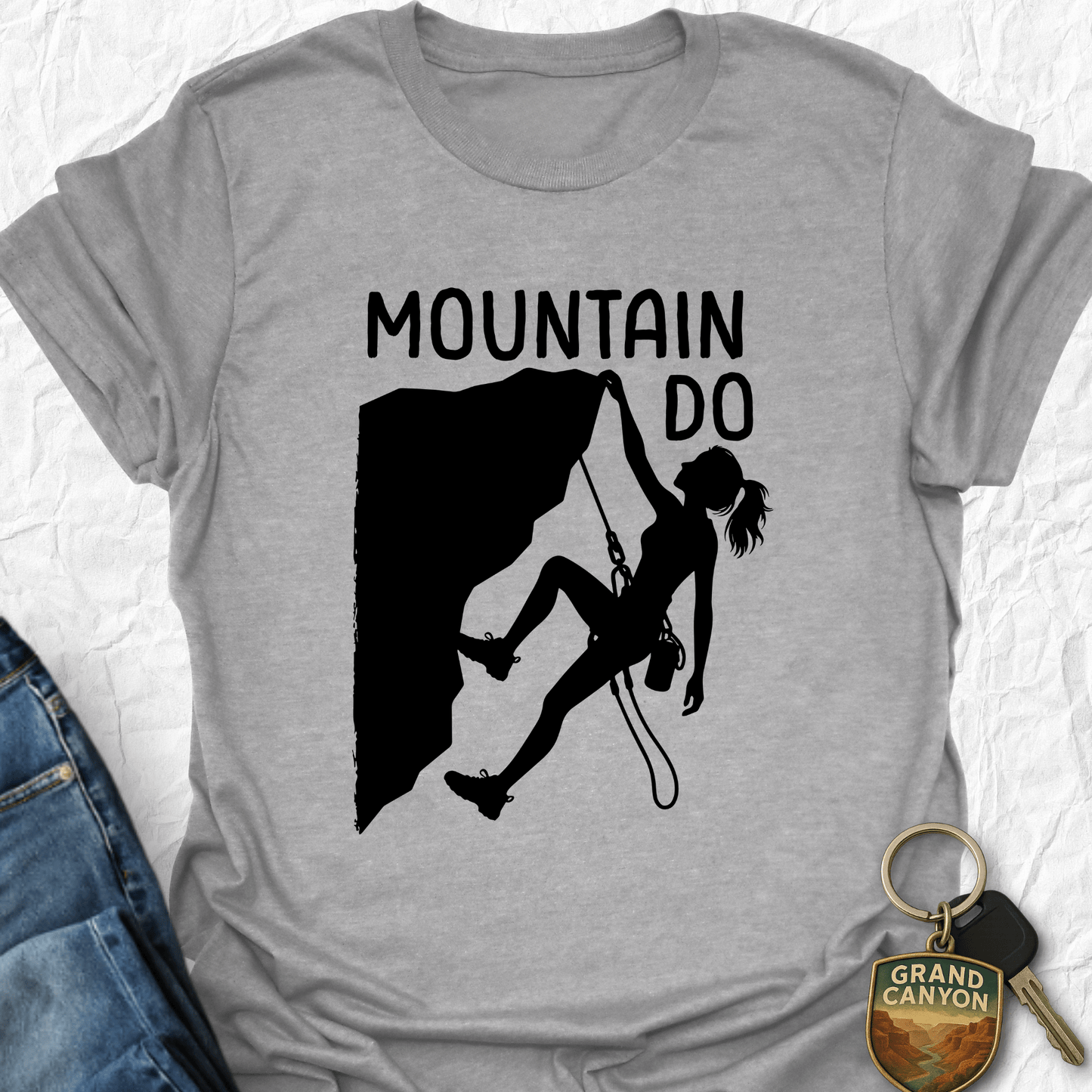 Gray t-shirt with mountain climbing graphic and 'Mountain Do' text, next to a keychain.