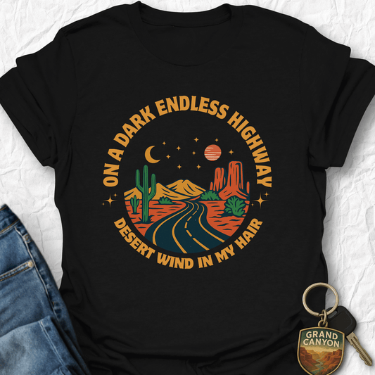 Black t-shirt with desert-themed graphic and text, paired with jeans and a keychain on a light background.