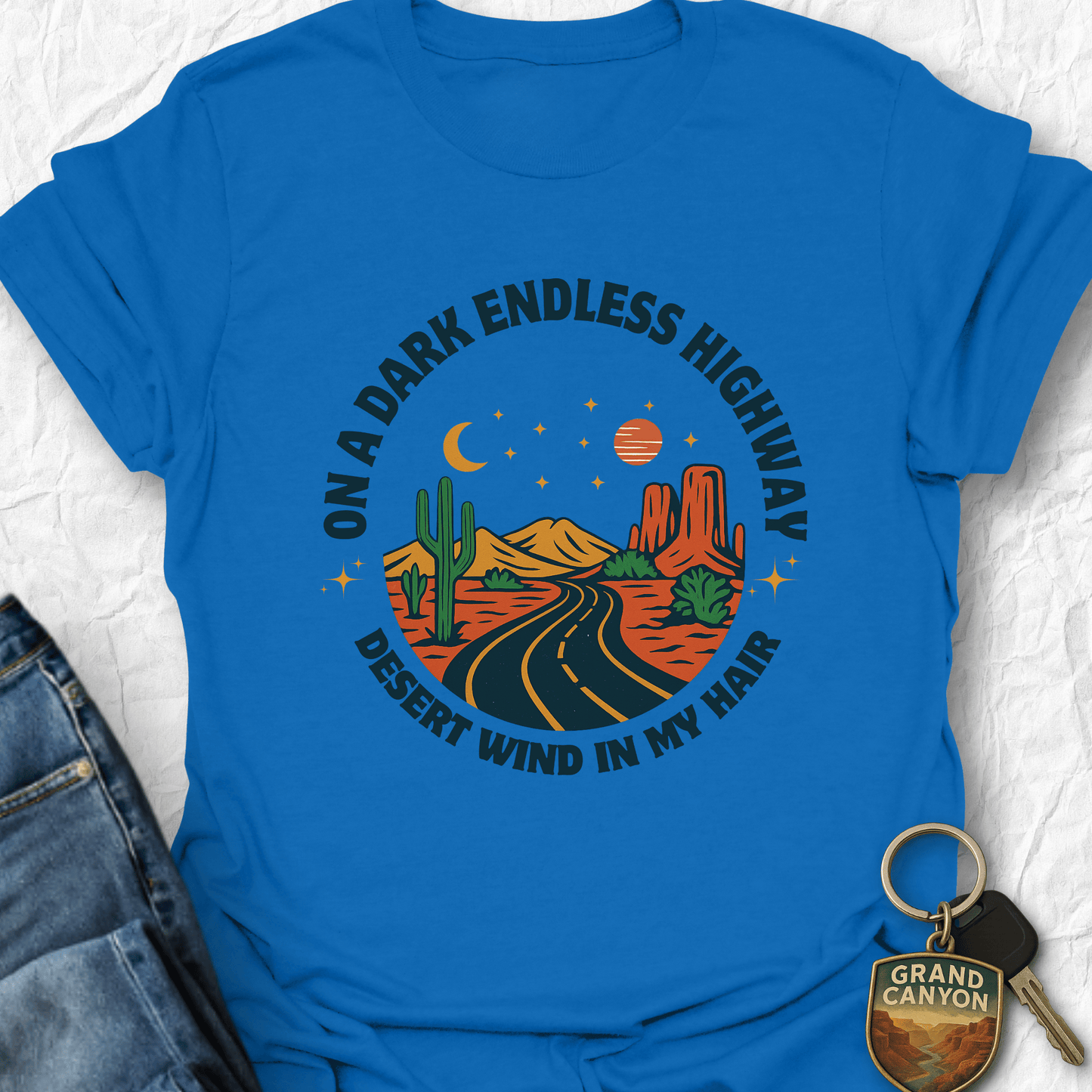 Blue t-shirt with desert-themed graphic and keychain on a textured white background
