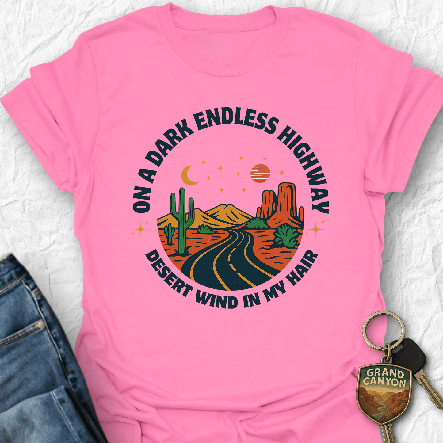 Pink t-shirt with desert-themed graphic and 'Grand Canyon' keychain on a textured surface