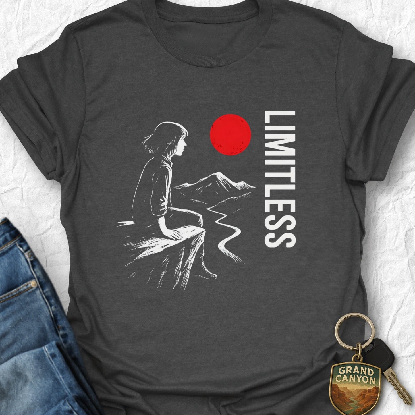 Gray t-shirt with a graphic of a person sitting on a cliff, a red circle, and the word 'LIMITLESS'.