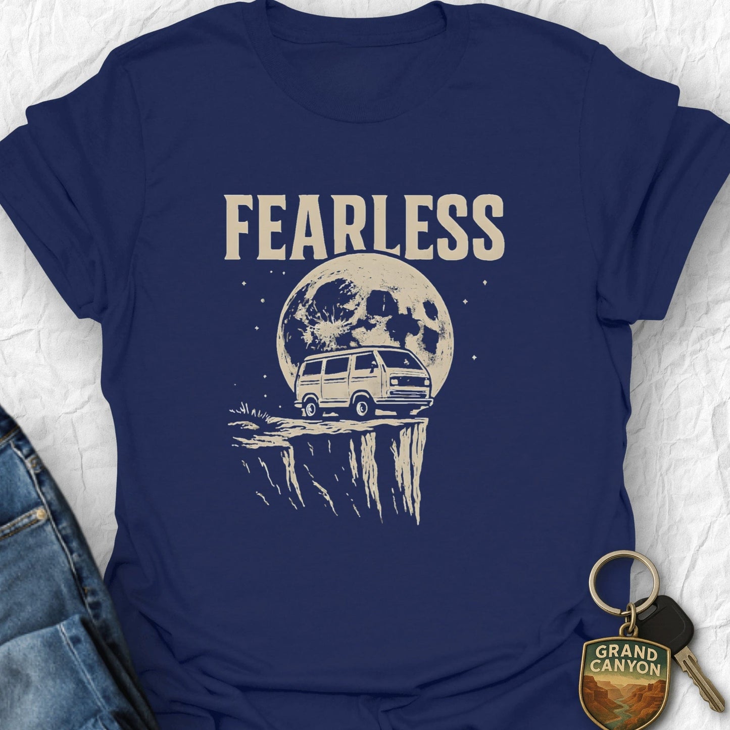 Navy blue t-shirt with 'FEARLESS' graphic and van under moon, next to jeans and keychain.