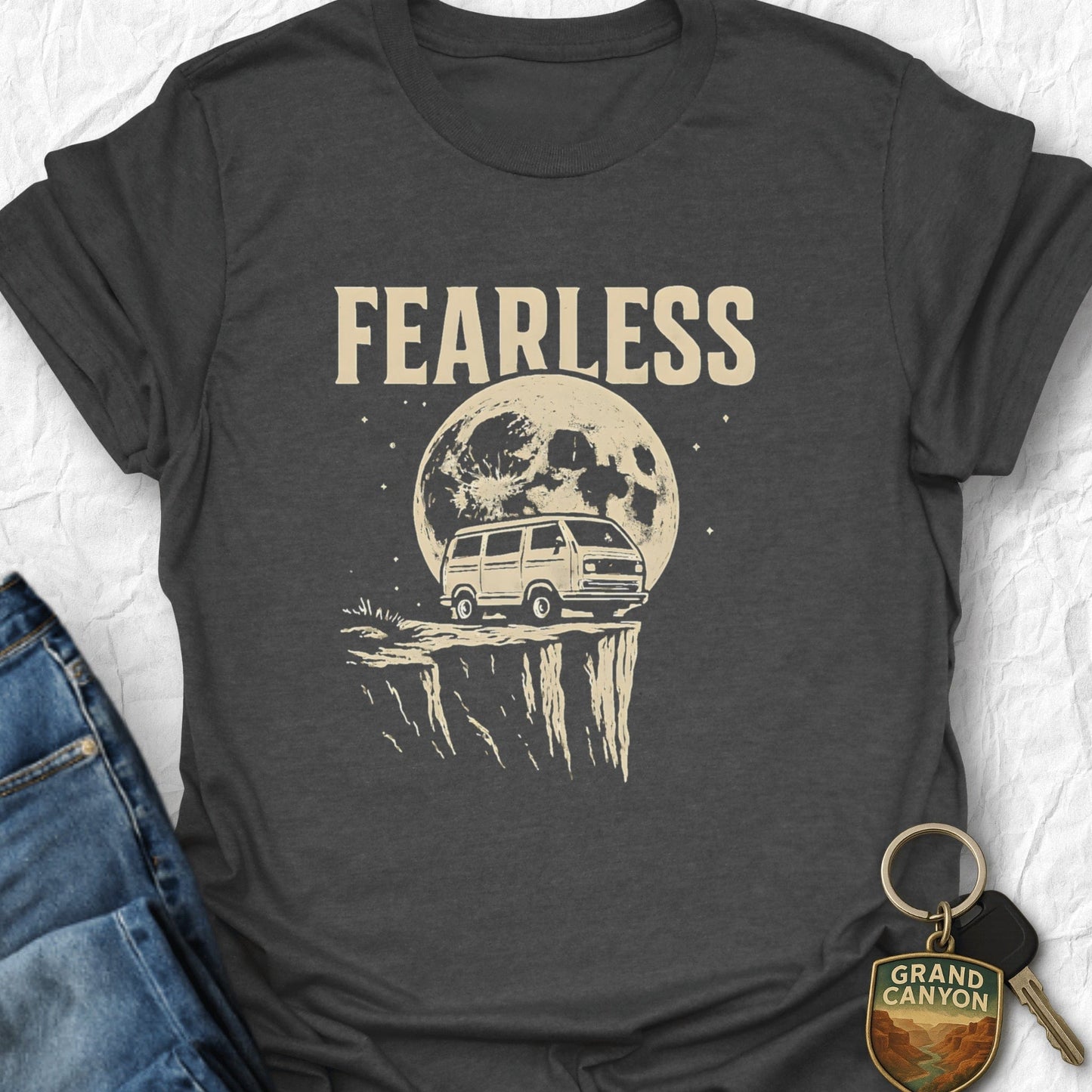 Dark gray t-shirt with 'FEARLESS' graphic design featuring a van and moon, displayed with jeans and a keychain.