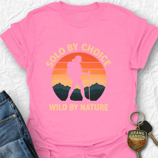 Pink t-shirt with 'Solo by choice, wild by nature' design on a textured surface with jeans and keys.