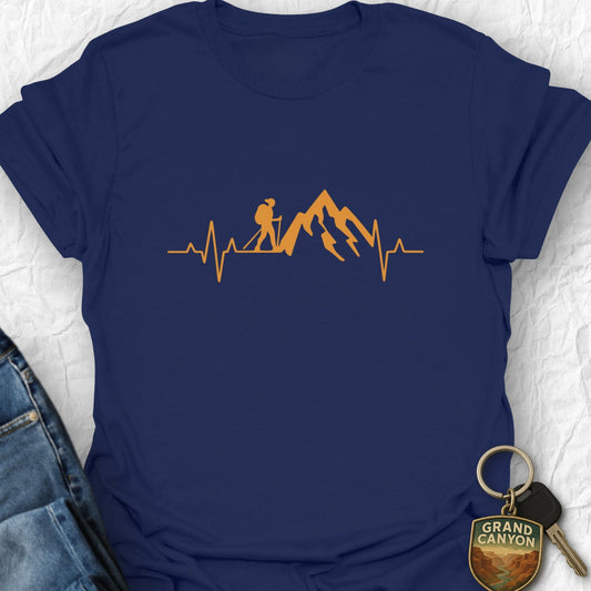 Navy blue t-shirt with orange heartbeat design featuring a hiker and mountains, placed on a white surface with jeans and a keychain.