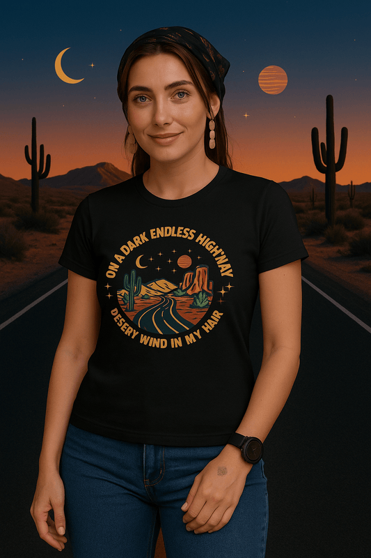 Woman wearing a black t-shirt with a desert-themed graphic and text, standing in front of a desert landscape with cacti and a sunset.